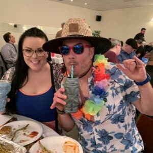 a man and women in Hawaiian shirts enjoying drinks at the trivia night