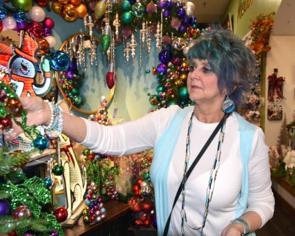 A woman with colorful hair and makeup decorating a christmas tree