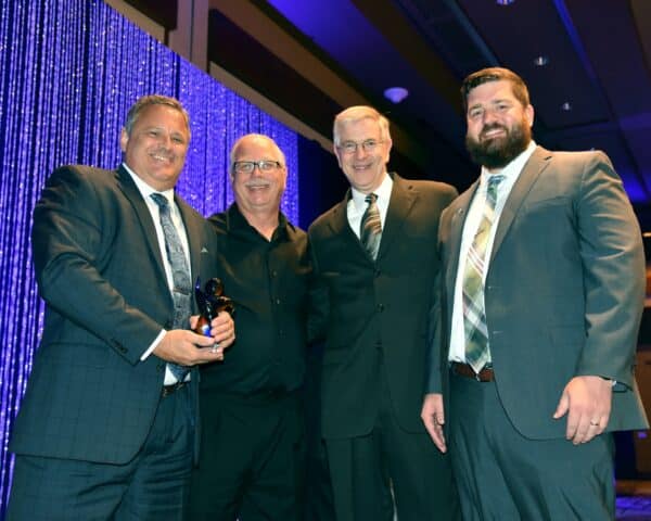 4 men smiling after receiving an award and holding the award statue