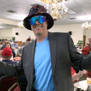 a man at a trivia night wearing a colorful hat and sunglasses