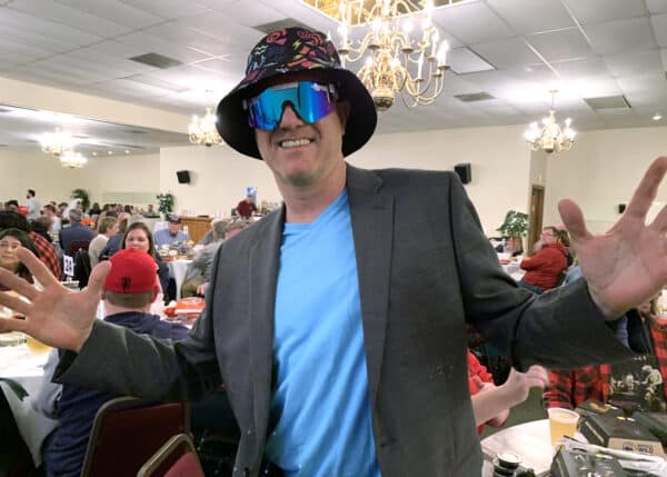 a man at a trivia night wearing a colorful hat and sunglasses